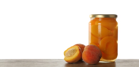 Photo of Glass jar of pickled peaches and fresh fruits on wooden table against white background. Space for text