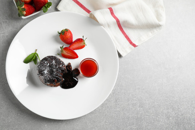 Photo of Delicious warm chocolate lava cake with mint and strawberries on grey table, flat lay