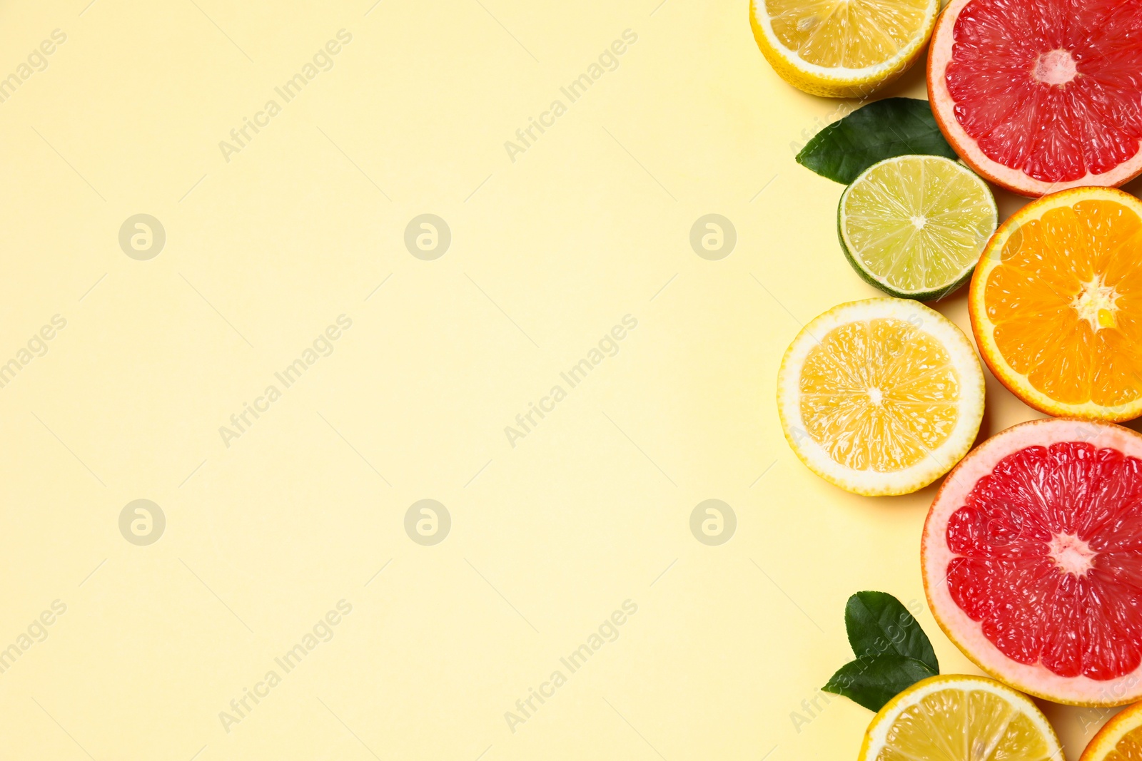 Photo of Different cut citrus fruits and leaves on beige table, flat lay. Space for text