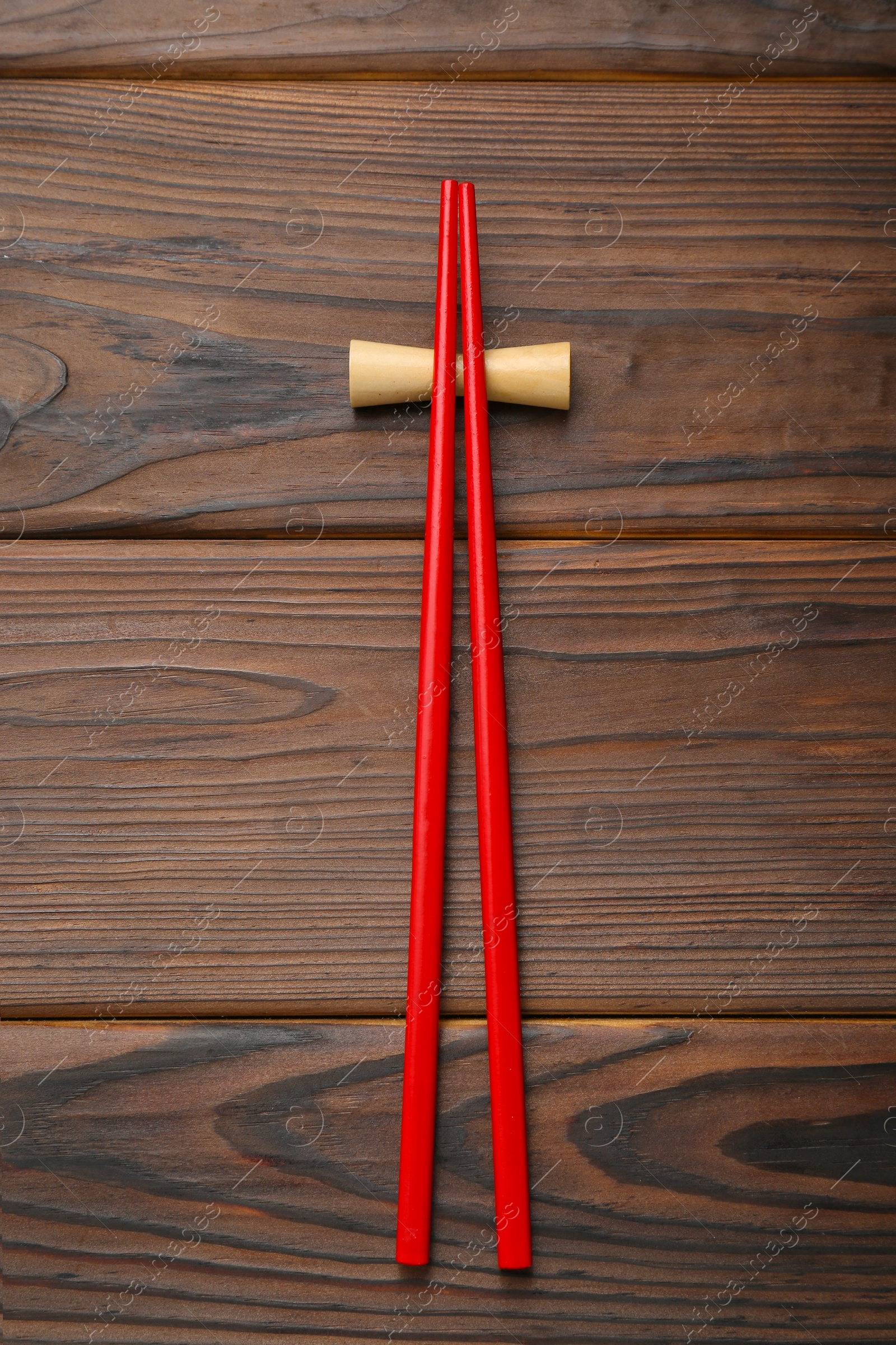 Photo of Pair of red chopsticks with rest on wooden table, top view