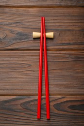 Photo of Pair of red chopsticks with rest on wooden table, top view