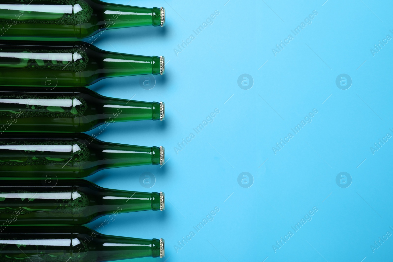 Photo of Bottles of beer on light blue background, flat lay. Space for text