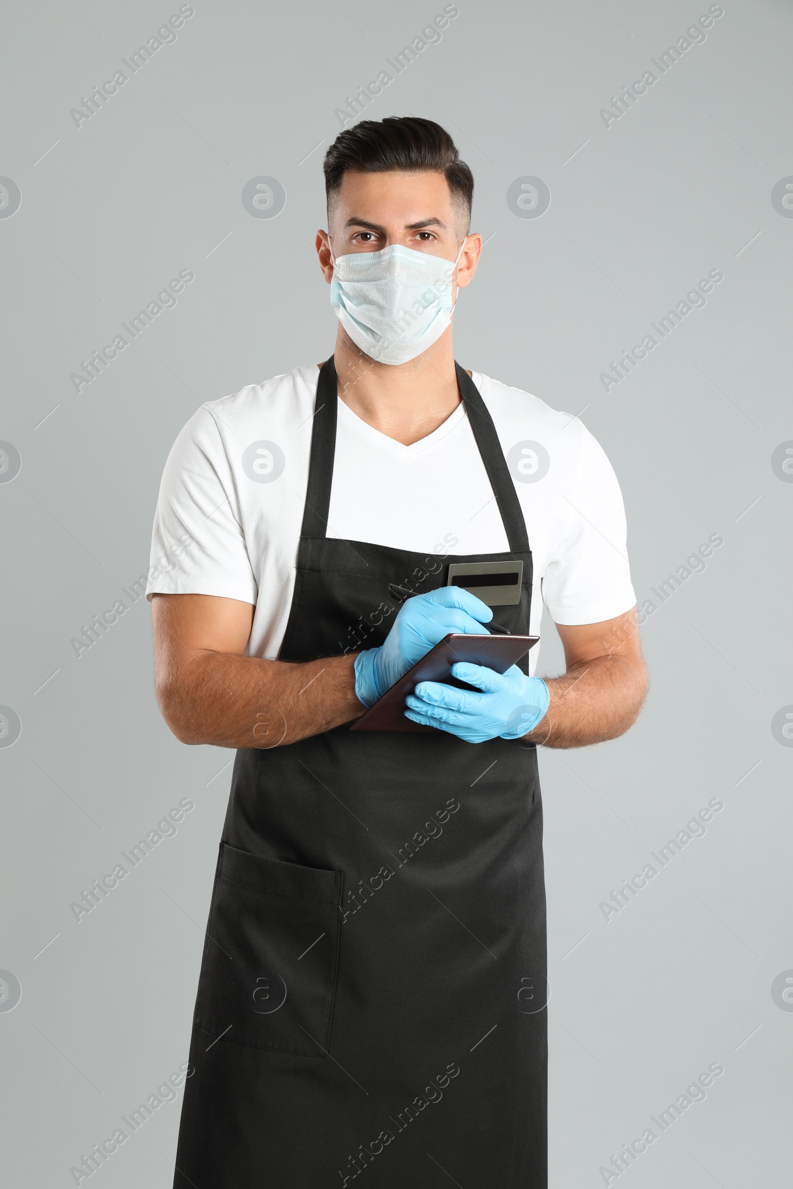 Photo of Waiter in medical face mask taking order on light grey background