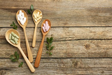 Vitamin capsules in spoons and leaves on wooden table, flat lay. Space for text