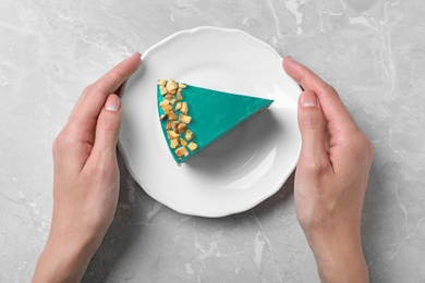 Woman holding plate with tasty spirulina cheesecake on grey background, top view