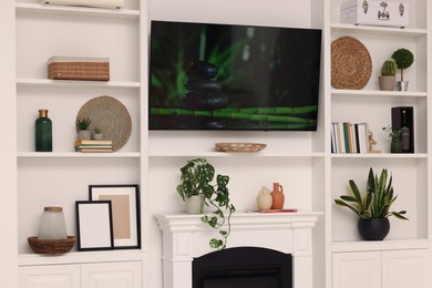 Photo of TV, fireplace and shelves with different decor in room. Interior design