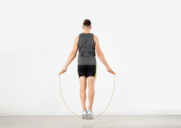 Photo of Sportive man training with jump rope in light room