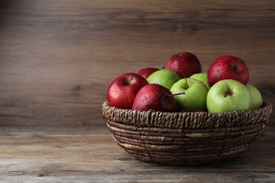 Fresh ripe green and red apples with water drops in wicker bowl on wooden table, space for text