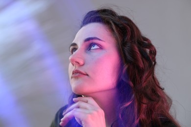 Photo of Fashionable portrait of beautiful young woman on grey background with colorful led lights, closeup
