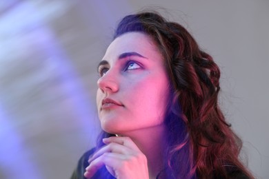 Fashionable portrait of beautiful young woman on grey background with colorful led lights, closeup