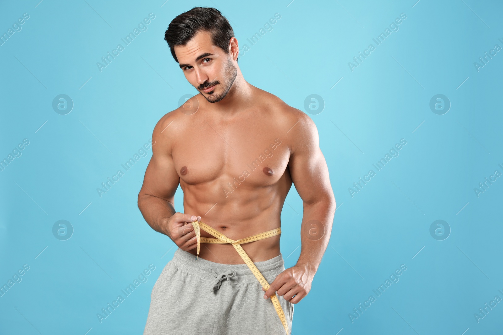 Photo of Young man with slim body using measuring tape on light blue background