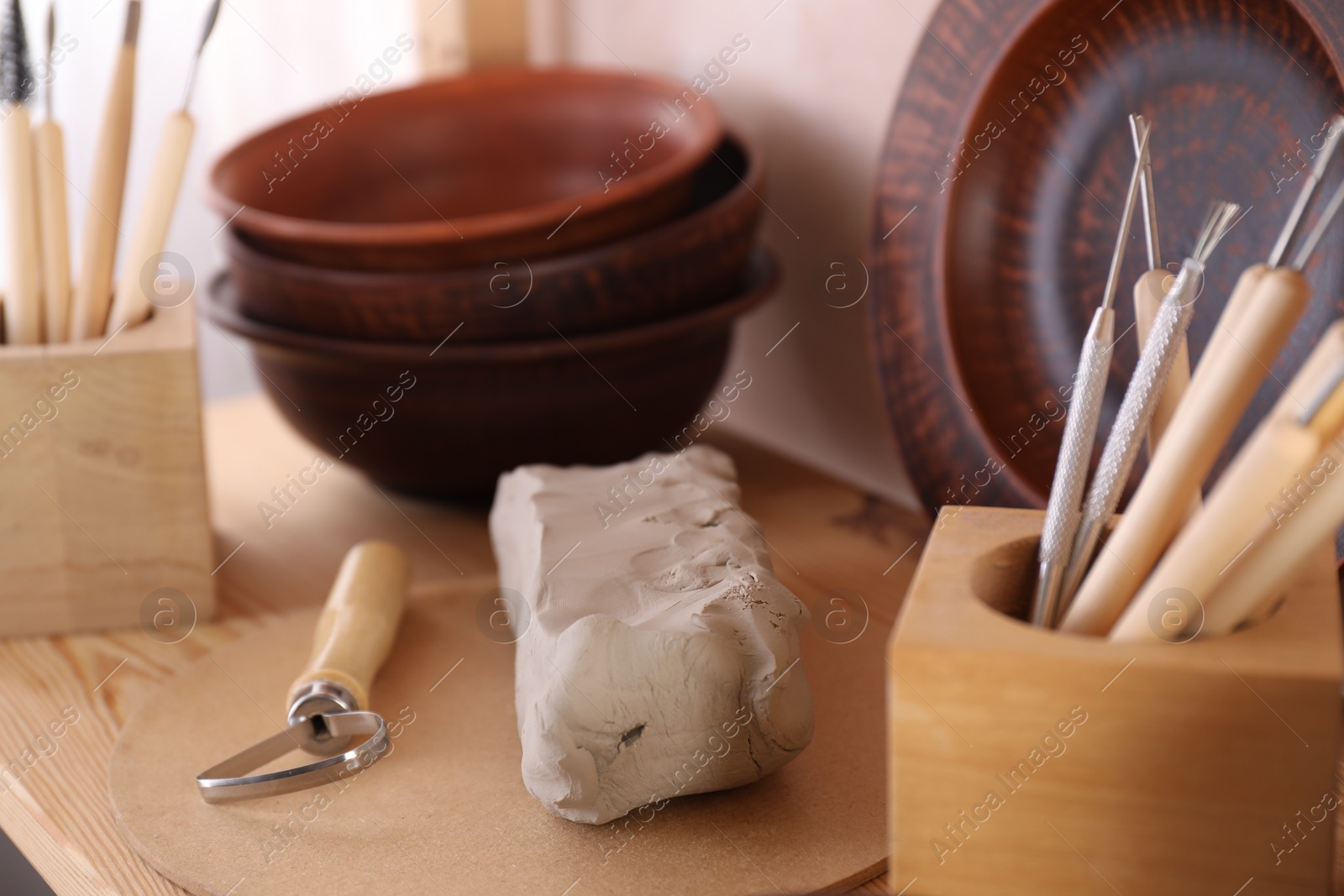 Photo of Set of different crafting tools and clay dishes on wooden table in workshop, closeup