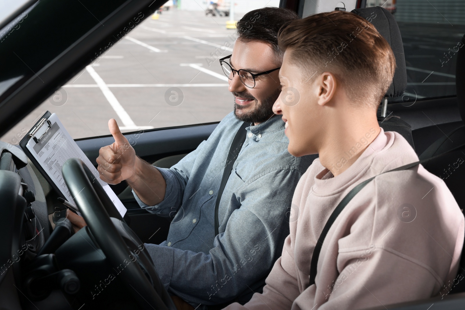 Photo of Driving school. Happy student passing driving test with examiner in car at parking lot