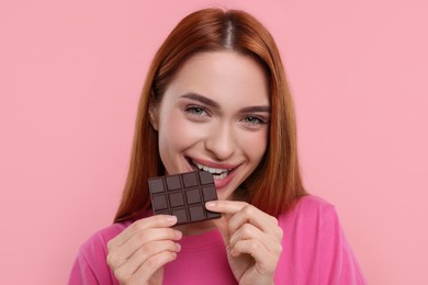 Photo of Young woman eating tasty chocolate on pink background