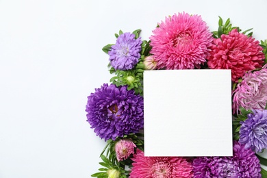 Photo of Beautiful aster flowers with sheet of paper on white background, top view. Space for text