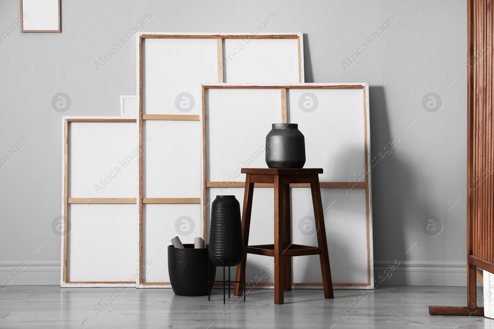 Photo of Many paintings, wooden stool and vases near grey wall in artist's studio