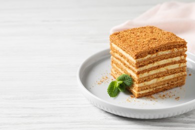 Photo of Slice of delicious layered honey cake with mint served on white wooden table. Space for text