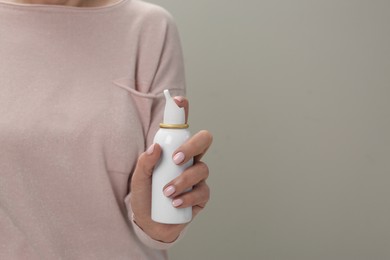 Photo of Woman holding nasal spray against light grey background, closeup. Space for text