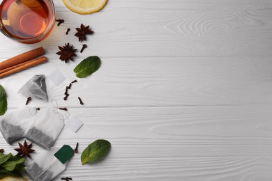 Tea bags, cup of hot drink and ingredients on white wooden table, flat lay. Space for text