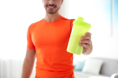 Young sporty man with bottle of protein shake at home, closeup