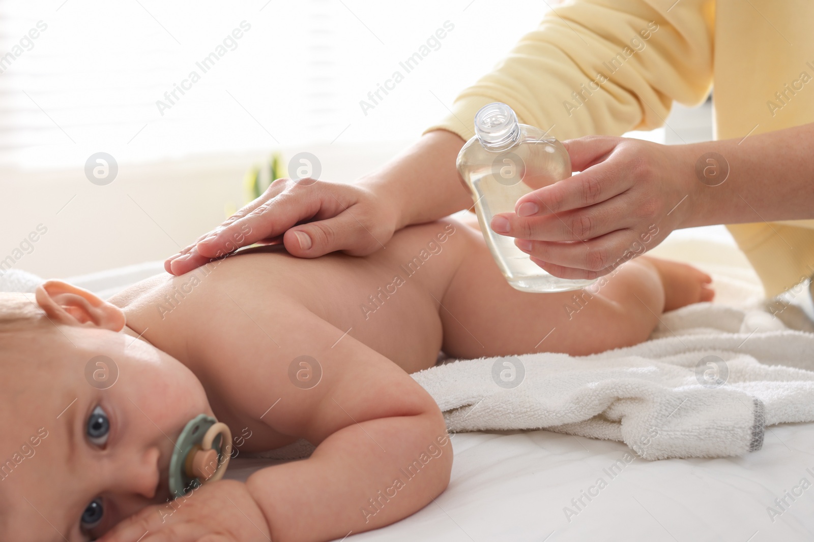 Photo of Mother massaging her cute baby with oil on bed at home, closeup