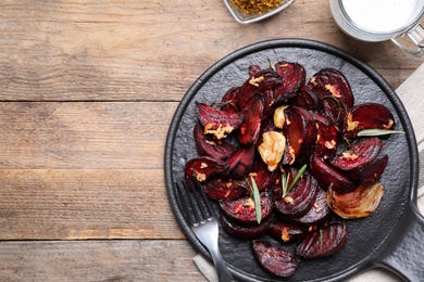 Photo of Roasted beetroot slices, garlic and rosemary on wooden table, flat lay. Space for text