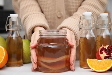 Photo of Woman taking jar of homemade fermented kombucha at white table, closeup