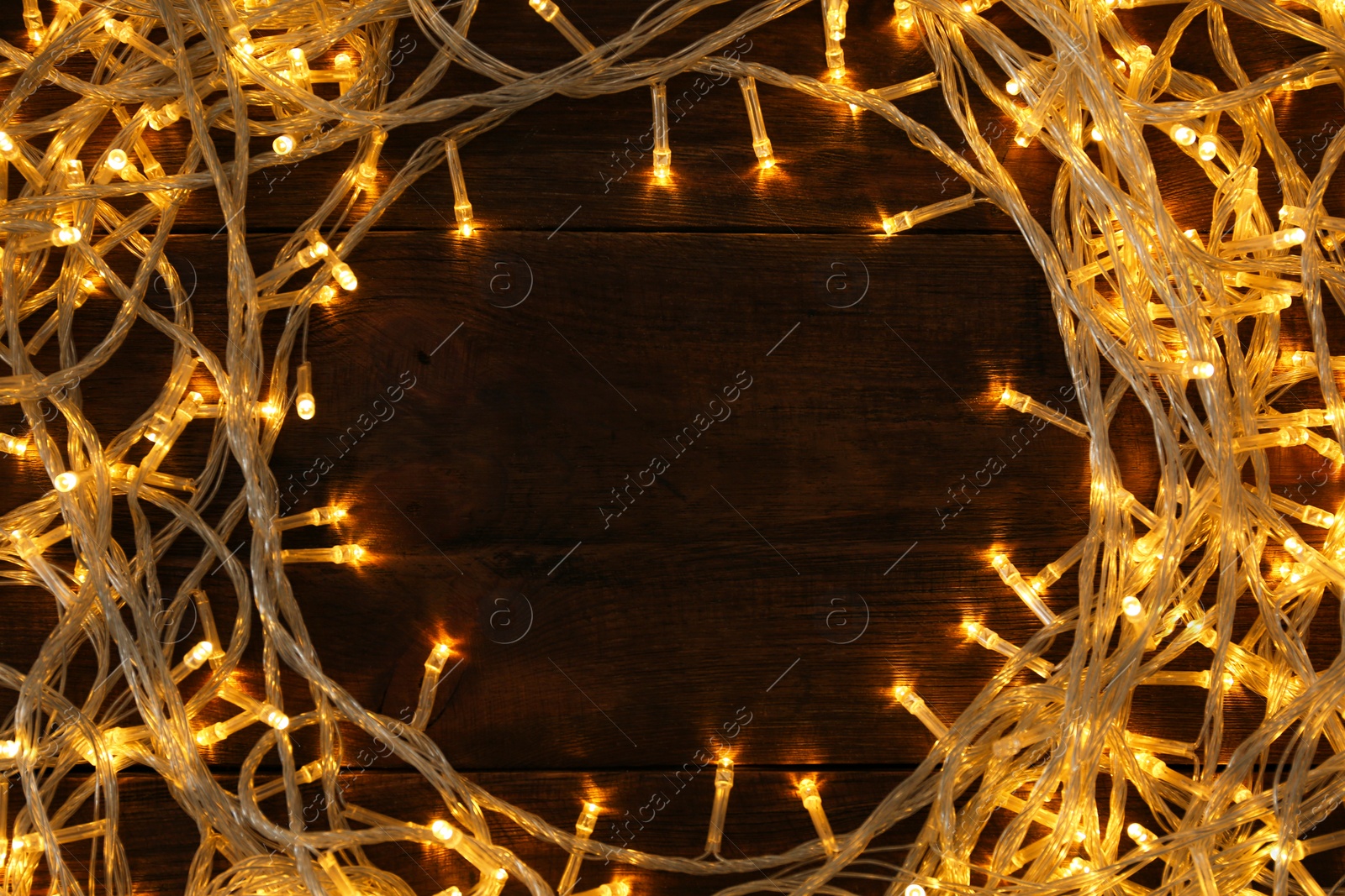 Photo of Frame made of glowing Christmas lights on wooden background, top view. Space for text