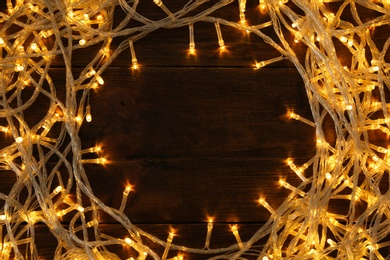 Frame made of glowing Christmas lights on wooden background, top view. Space for text