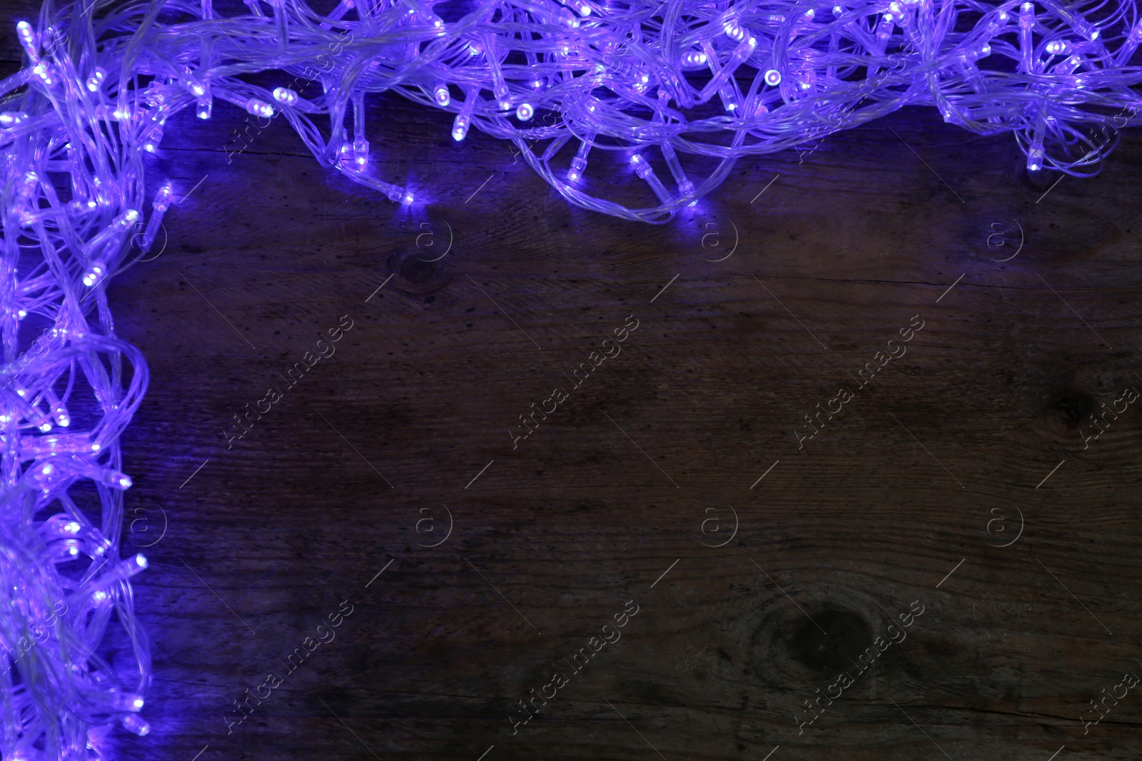 Photo of Frame made of blue Christmas lights on wooden background, top view. Space for text