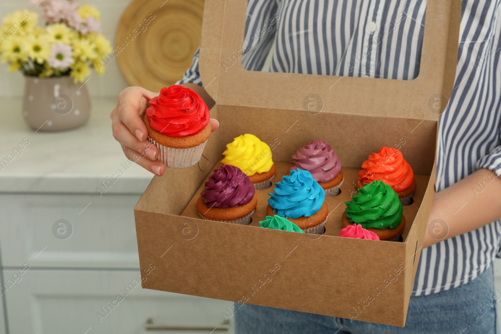 Photo of Woman holding box with delicious colorful cupcakes indoors, closeup