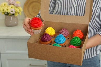 Photo of Woman holding box with delicious colorful cupcakes indoors, closeup