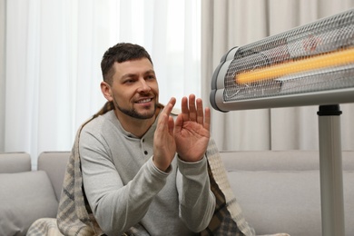 Man warming hands near electric infrared heater at home