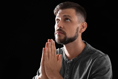 Photo of Man with hands clasped together for prayer on black background. Space for text