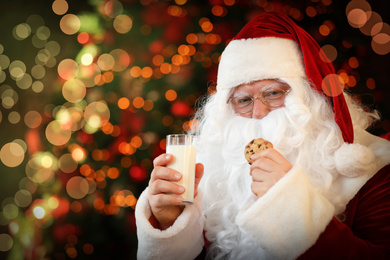 Photo of Santa Claus with milk and cookie near Christmas tree indoors