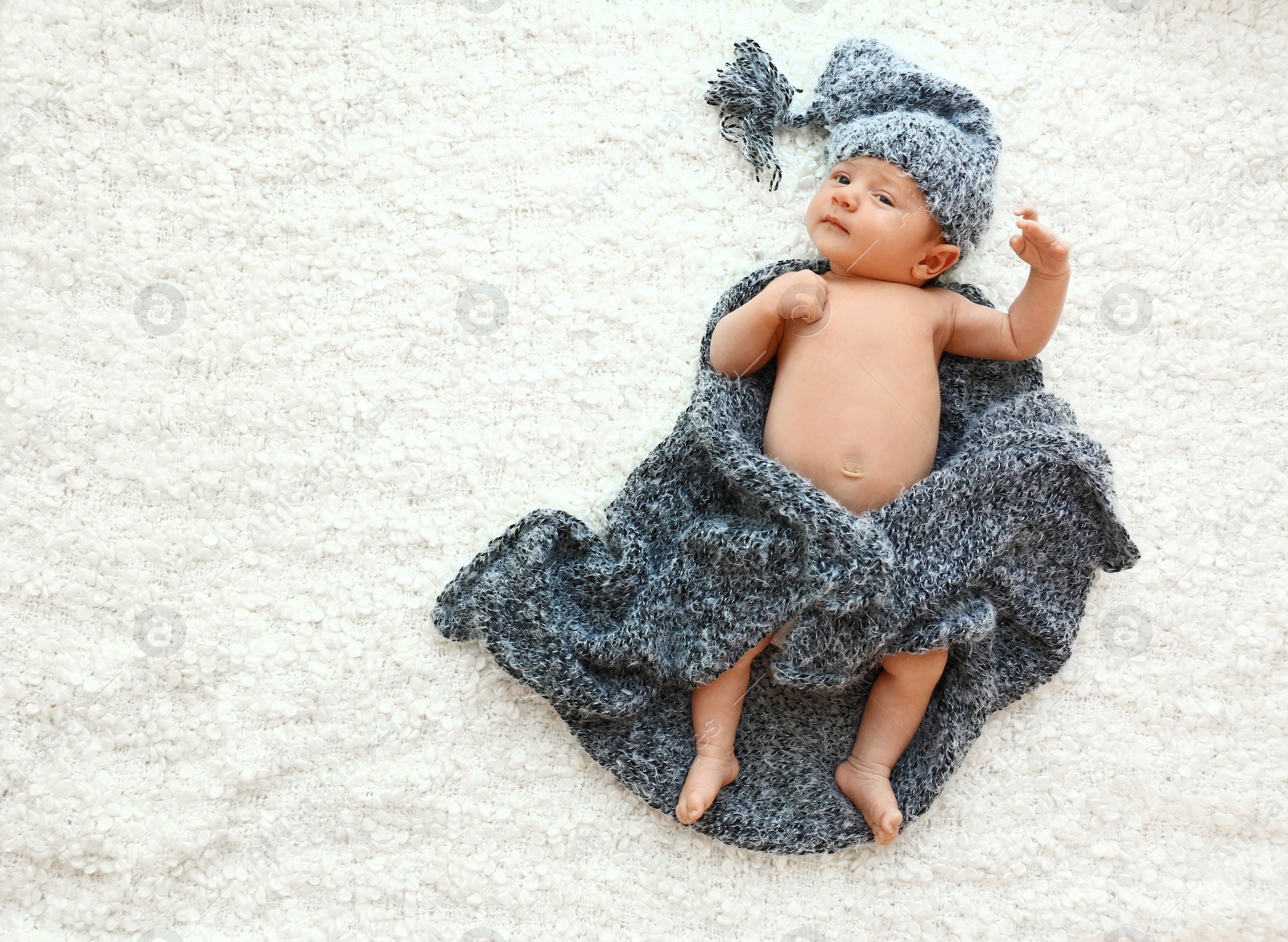 Photo of Cute little baby in grey hat and plaid lying on soft blanket, top view. Space for text