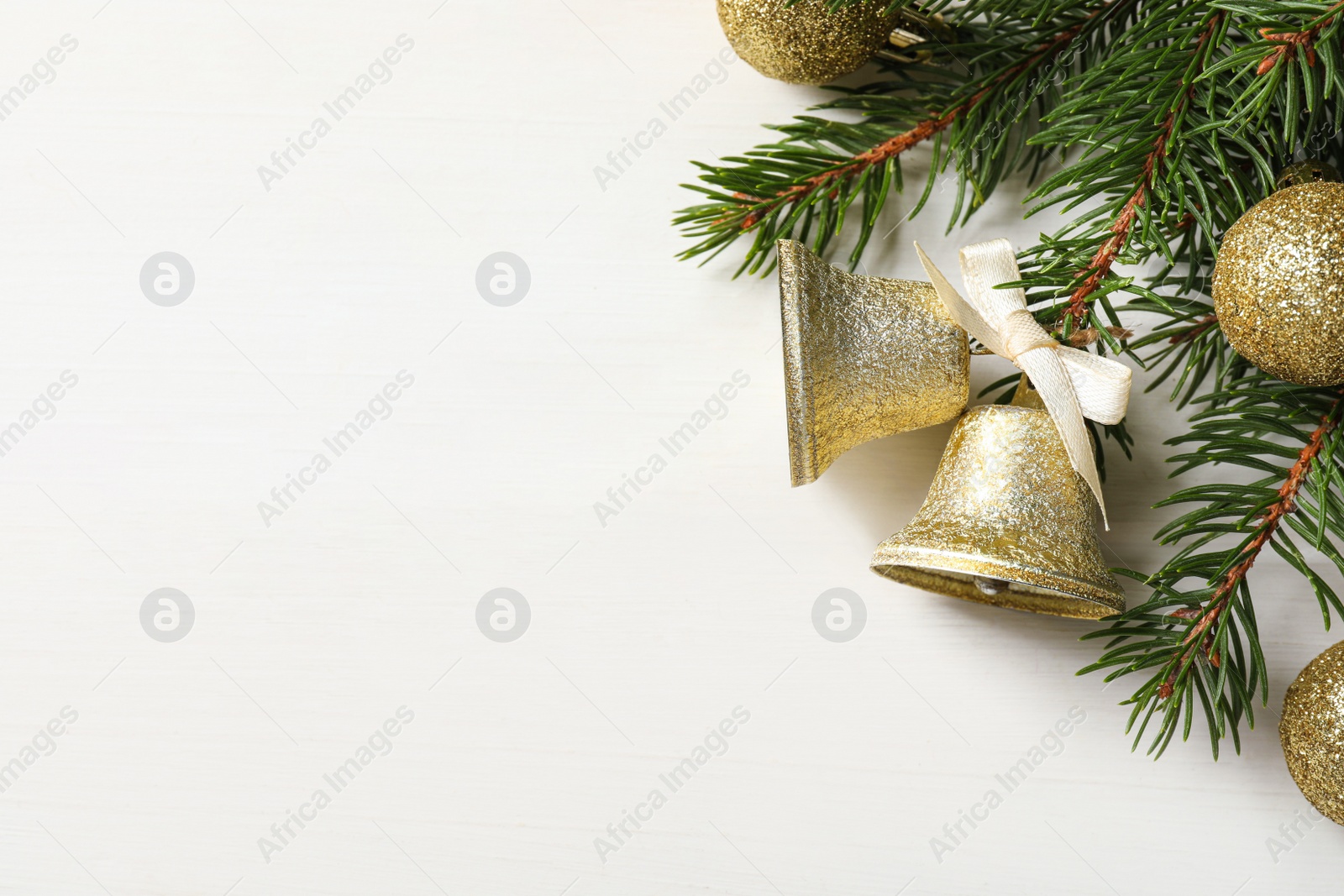 Photo of Christmas bells and fir tree branches on white wooden table, flat lay. Space for text