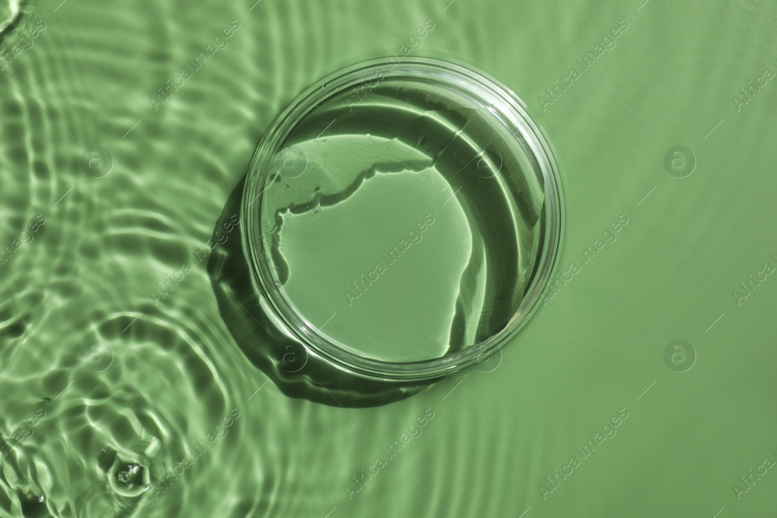 Photo of Stylish presentation for product. Glass podium in water on pale green background, top view