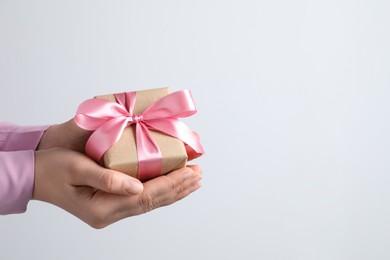Photo of Woman holding gift box with pink bow near white wall, closeup. Space for text
