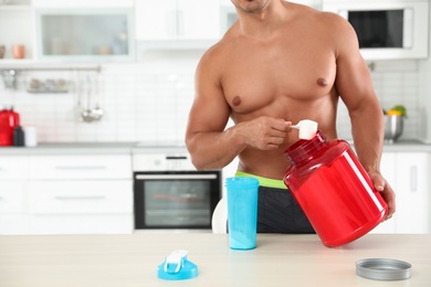 Young athletic man preparing protein shake in kitchen, closeup view. Space for text
