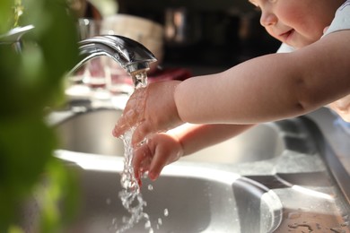 Photo of Little child washing hands in kitchen, closeup view