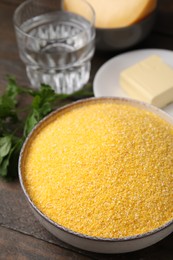 Raw cornmeal in bowl, water and butter on wooden table, closeup