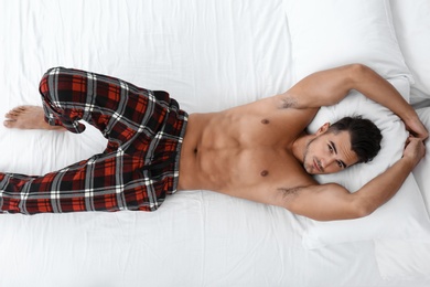 Sexy young man lying on bed with soft pillows at home, top view