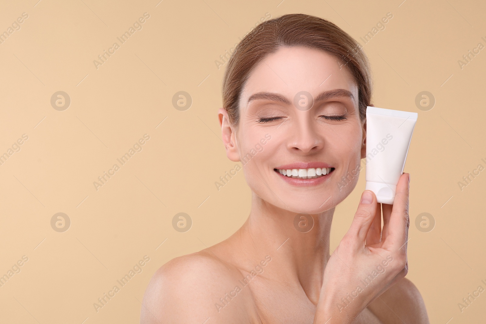 Photo of Woman holding tube of foundation on beige background. Space for text