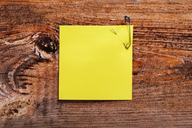 Photo of Yellow paper note attached with safety pin on wooden table, top view. Space for text