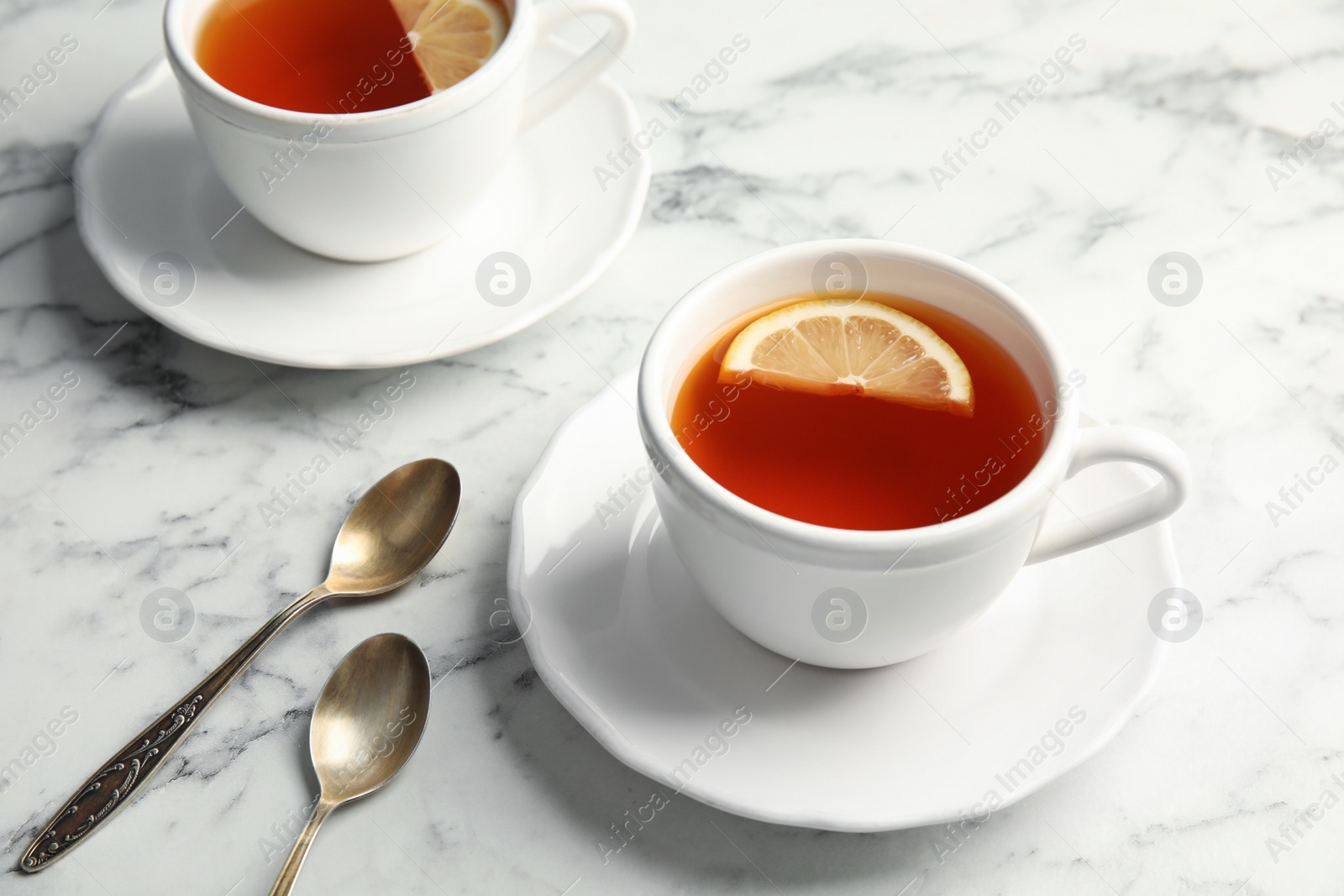 Photo of Cups with black tea and lemon on marble table