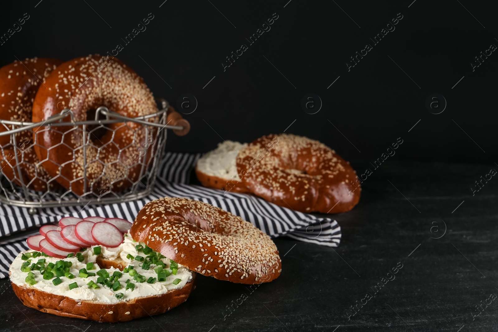 Photo of Delicious bagel with cream cheese, radish and green onion on black table. Space for text