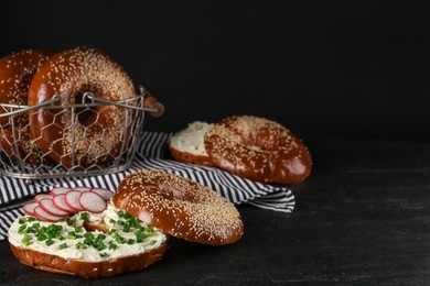 Photo of Delicious bagel with cream cheese, radish and green onion on black table. Space for text