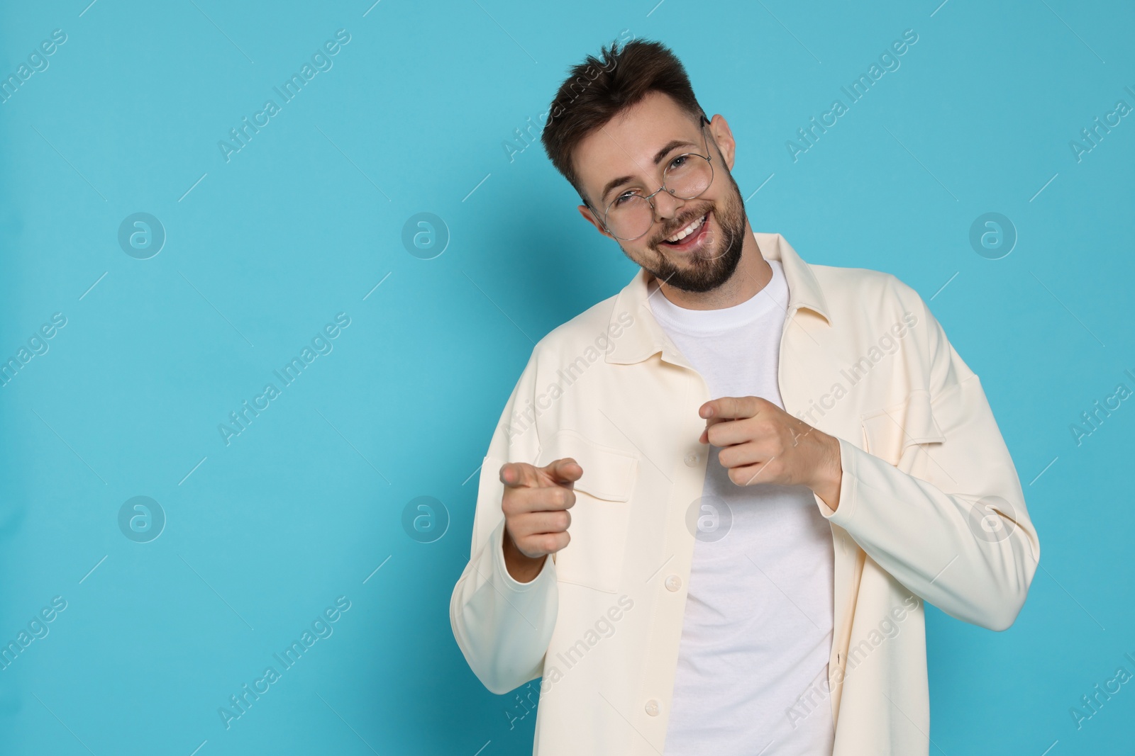 Photo of Handsome man in white jacket pointing fingers on light blue background, space for text