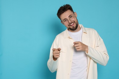 Handsome man in white jacket pointing fingers on light blue background, space for text